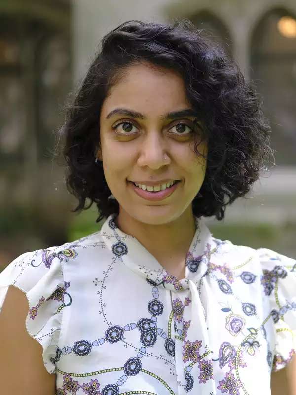 Professor Shukla gently smiles at the camera. She is wearing a white short-sleeved blouse that has blue and pink flowers decorating it. Her hair is in a side-swept bob, which goes a bit past her chin.